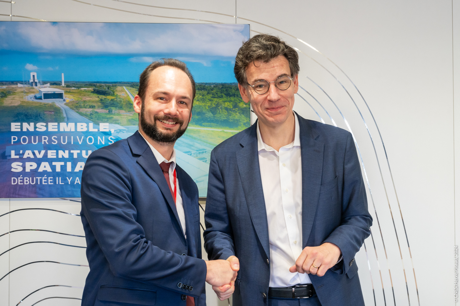 HyPrSpace CEO shaking hands with a CNES representative in front of a poster about European space exploration, symbolizing institutional partnership and support.