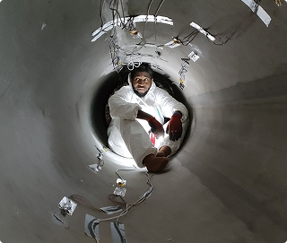 HyPrSpace technician sitting inside a large cylindrical tank, wearing a clean suit. A behind-the-scenes look at the physical scale and complexity of aerospace development.