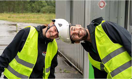 Two smiling HyPrSpace team members in high-visibility vests and helmets, leaning their heads together playfully, embodying the team’s unity and positive energy on the field.